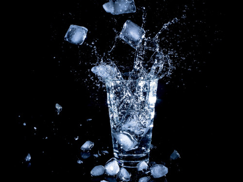 Ice cubes dropped in clear drinking cup of water.