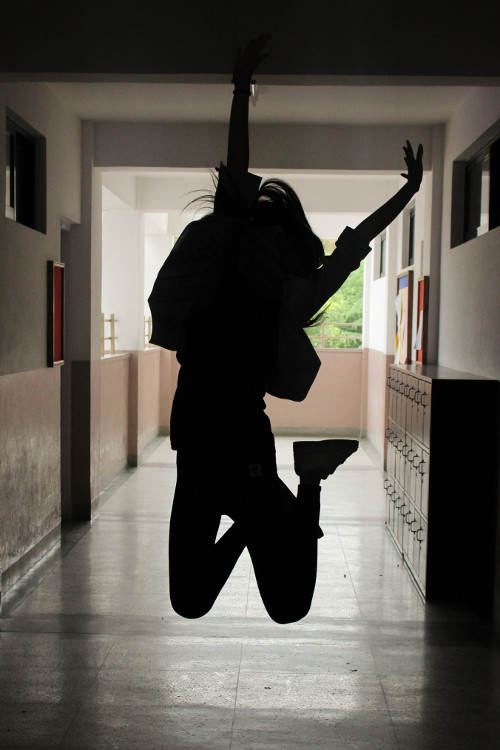 Silhueta de uma mulher fazendo uma pose de pulo em um corredor de uma escola.