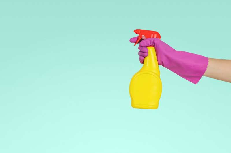 Photo of an arm with a glove holding a cleaning product.
